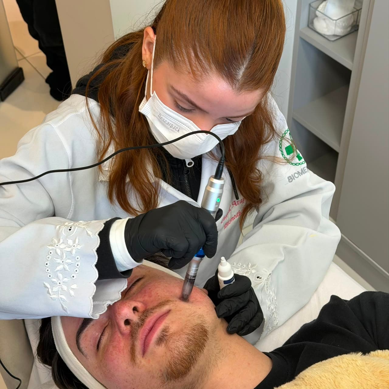 Aluna do SkinLab aplicando microagulhamento na face de um paciente, com a caneta apoiada na bochecha.